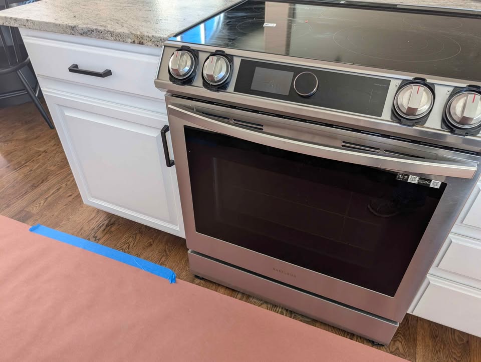 White kitchen cabinets with stove, microwave, dishwasher and countertops.